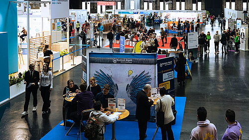 Blick in eine Messehalle mit Messeständen und Besuchern